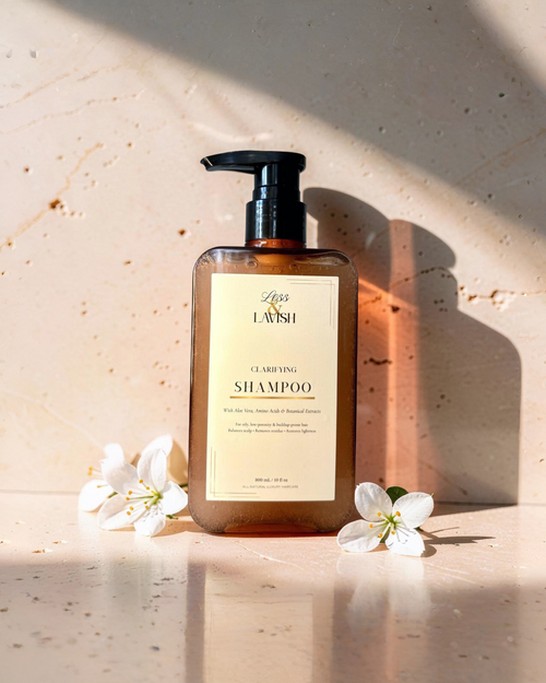 Less & Lavish Clarifying Shampoo bottle on a light wooden surface with flowers.